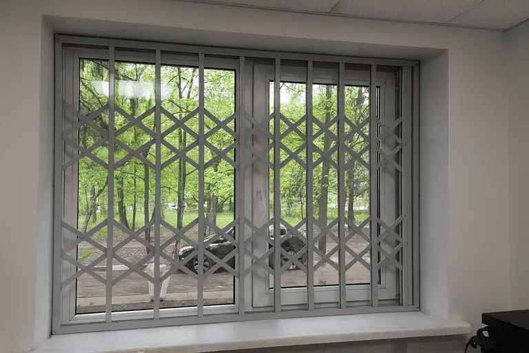 Белые раздвижные решётки на пластиковом окне, вид на зелёный двор